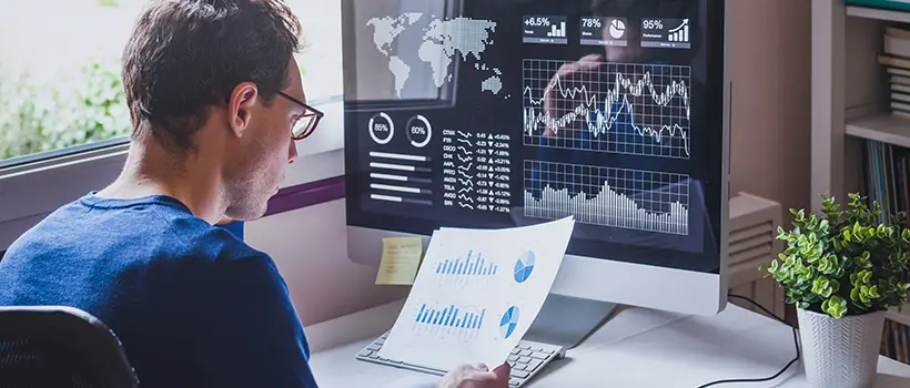 An individual sitting at their desk reviewing stock graphs on a printout. 